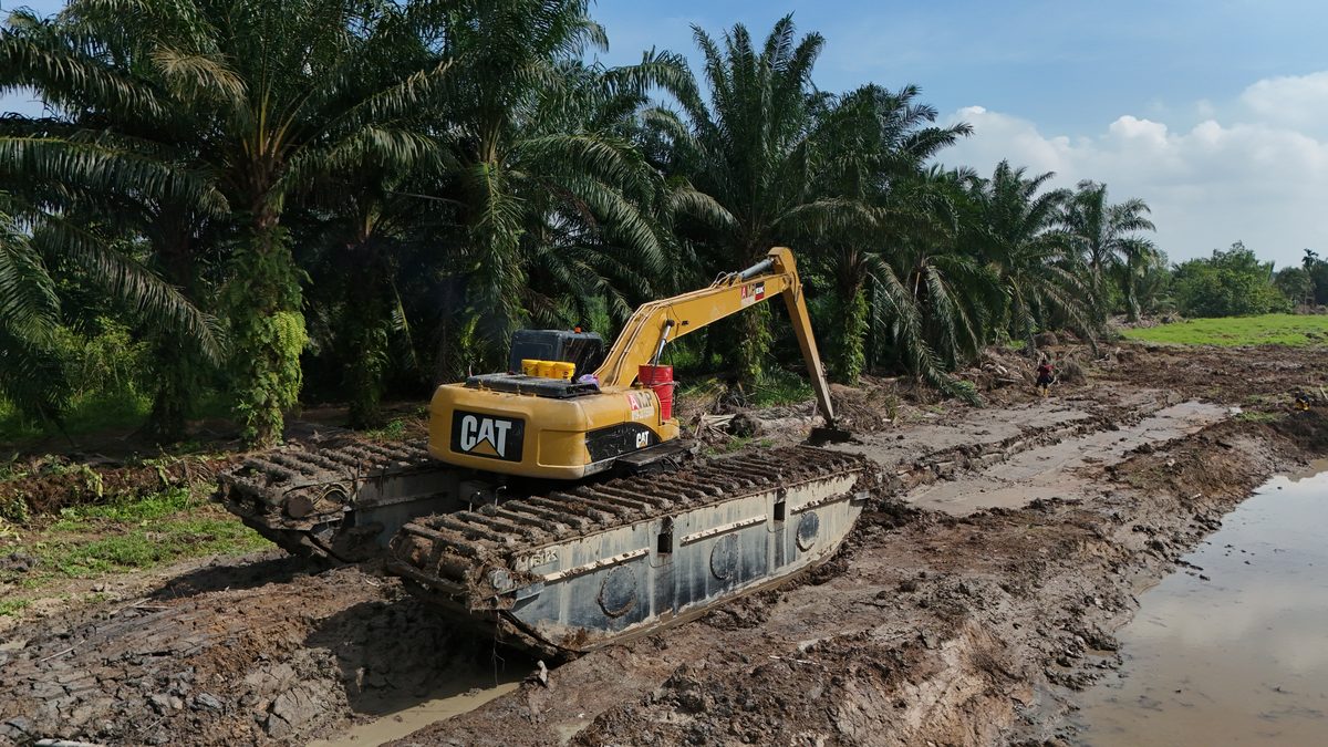 Long-reach excavator on pontoon tracks working a flood channel between oil palm