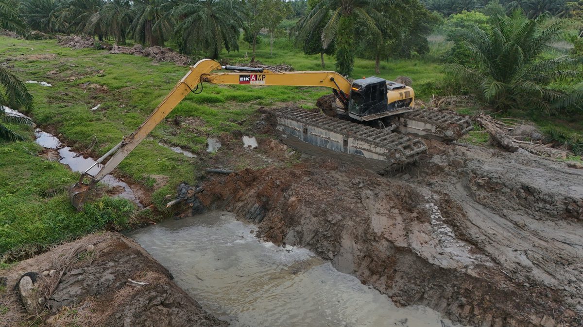 Long-reach excavator dredging a flooded channel from its bank